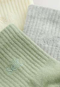 Három pár bordázott zokni: halványsárga, világosszürke és tompa zöld, mindegyiken az azonos színű "self" logó hímzéssel. Puha, texturált anyag.