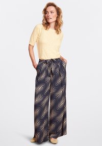 Geel gebreid top met een getextureerd patroon; losse marineblauwe broek met een golvend beige ontwerp en tailleband detail.