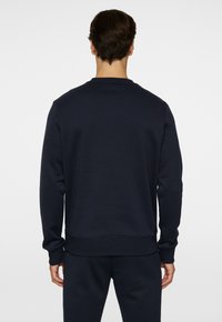 Mörkblå crewneck sweatshirt tillverkad av mjukt tyg, med ribbade manschetter och nederkant, samt en slät textur och minimalistisk design.