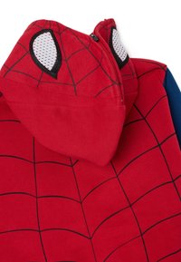 Sudadera roja con diseño de Spider-Man, que presenta un patrón de telaraña negra, acentos de malla en los ojos y un cierre de cremallera. Manga azul en un lado.