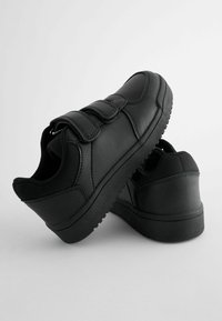 Une paire de baskets noires pour enfants avec des bandes Velcro, des semelles texturées et des cols rembourrés sur un fond neutre.