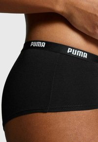 Schwarze Baumwollunterwäsche mit einem gebrandeten Bündchen, auf dem das Wort "PUMA" in Weiß steht. Glatte Textur und figurbetontes Design.