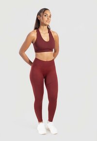 Sujeción deportiva burdeos y leggings de cintura alta hechos de tela elástica, combinados con zapatillas deportivas blancas. Textura suave, diseño minimalista.