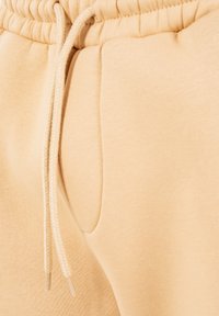 Vita di pantaloni sportivi beige con fascia elastica, coulisse e tasca laterale che mostra la trama del tessuto e i dettagli delle cuciture.