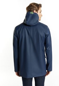 Jachetă impermeabilă de culoare bleumarin, cu guler înalt, design fără cusături și etichetă pe spate. Prezintă mâneci lungi și un croi drept.