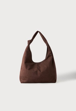 Braune strukturierte Stoffhandtasche mit einem einzelnen Griff, der zu einem Knoten gebunden ist, vor einem einfachen hellen Hintergrund dargestellt.