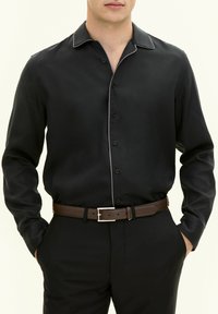 Maglietta nera a maniche lunghe con colletto a punta e piping bianco a contrasto. Presenta bottoni sul davanti e una texture del tessuto liscia.