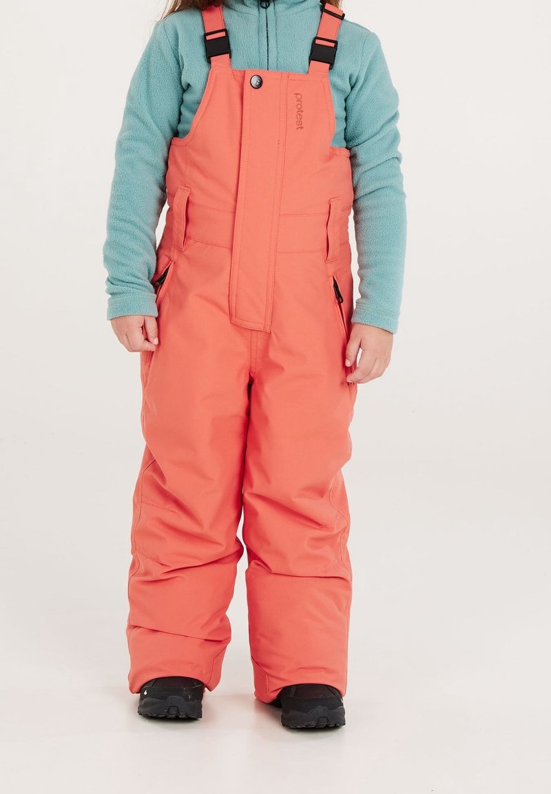 Pantaloni da neve color corallo con spalline regolabili, tasche laterali e polsini rinforzati, abbinati a un maglione in pile azzurro chiaro e stivali neri.