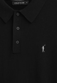 Svart polo skjorta i stickad tyg, med krage och tre knappar. Inkluderar en liten vit broderad logotyp av en golfspelare.