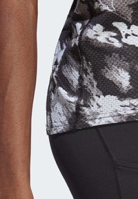 Camiseta deportiva con un patrón en blanco y negro y una superficie texturizada, mostrada junto a leggings negros lisos con costuras en contraste.