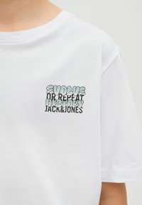 Balta 100% medvilnės marškinėliai su apvaliu kaklu. Priekyje juoda ir mėlyna spalvomis užrašyta: „EVOLIUOK ARBA PAKARTOK ISTORIJĄ JACK&JONES.“ Trumpi rankoviai.