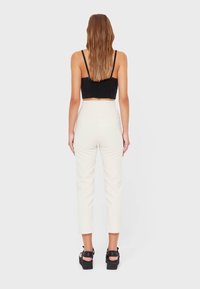 Zwarte cropped top van textuur materiaal, gecombineerd met crème hoge taille broeken. Model draagt zwarte platform sandalen. Eenvoudige witte achtergrond.