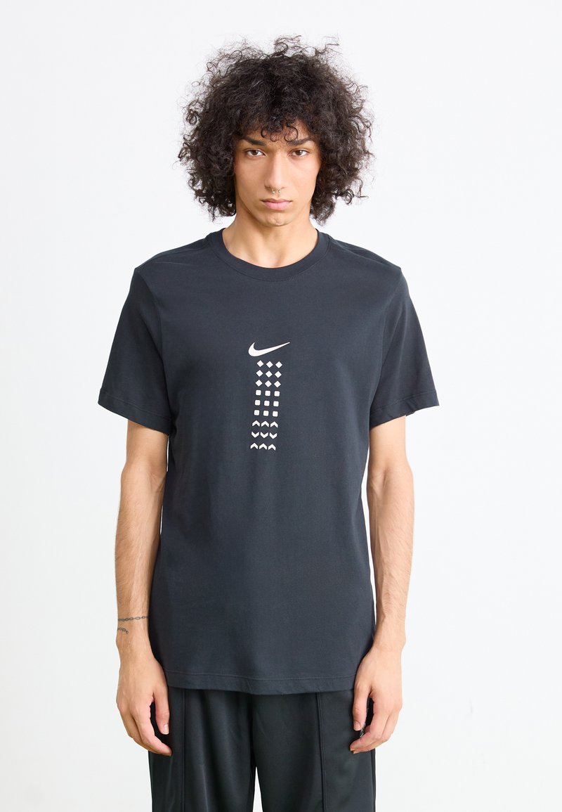 Juodas medvilnės marškinėlis su apvalia iškirpte, ant priekinės pusės esantis baltas Nike logotipas ir geometriniai raštai, kurie yra įvairių formų ir dydžių.