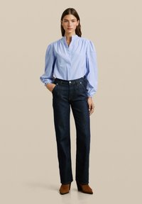 Lichtblauw gestreept blouse met opgezette mouwen, hoge kraag, gecombineerd met donkerdenim, hoge taillebroek en bruine haklaarzen.