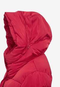 Chaqueta acolchada roja con una capucha grande y estructurada, cierre de cremallera y textura suave y brillante. Diseñada para proporcionar calor y comodidad.