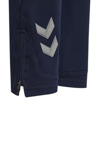 Marina idrottsbyxor i texturerat tyg, med en ficka med dragkedja och två ljusgrå chevronmönster nära fållen.