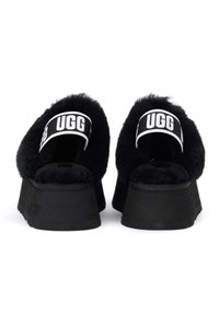 Sandalias de plataforma negras con una textura esponjosa y punta abierta. Cuenta con una tira de marca con "UGG" en blanco y una suela de goma gruesa.