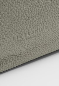 Gros plan sur un matériau en cuir gris texturé avec le nom de la marque embossé "LIEBESKIND BERLIN" sur la surface.