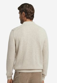 Beżowy sweter z dzianiny z wysokim kołnierzem. Ma ribbowe mankiety i dół, teksturowane detale na ramionach oraz miękki, przytulny wygląd.