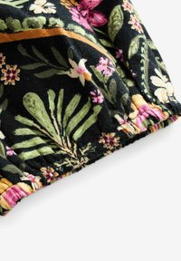 Blommigt tyg med en mängd färgglada blommor och gröna blad på en svart bakgrund, med samlade kanter och en texturerad yta.