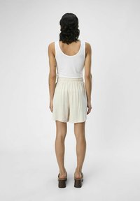 Lettere cremede shorts med en tekstureret overflade, der har et elastisk taljebånd, parret med en hvid tanktop og klodsede hæle sandaler.