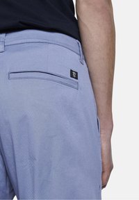 Pantaloni azzurri chiari con una texture morbida, dotati di una tasca posteriore e di un piccolo etichetta nera. L'elastico in vita è visibile, accentuando il design.