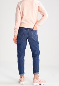 Světle růžová mikina, modré džínové kalhoty s ohrnutými manžetami a světle růžové tenisky, předvádějící ležérní a uvolněný střih a měkkou látku.