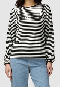 Haut à manches longues rayé noir et blanc avec un col rond et un détail en texte pailleté, associé à un jean bleu clair orné.