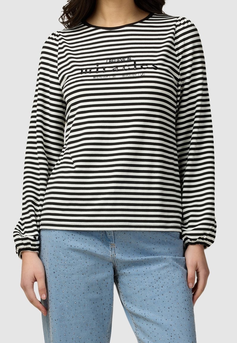 Haut à manches longues rayé noir et blanc avec un col rond et un détail en texte pailleté, associé à un jean bleu clair orné.