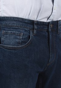 Muške tamnoplave traperice klasičnog kroja s vidljivim stražnjim džepom i suptilnim detaljima šivanja, osmišljene za ležeran izgled.