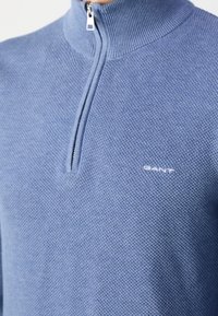 Hellblau gestrickter Viertel-Reißverschluss-Pullover aus strukturiertem Stoff mit geripptem Kragen. Mit kleinem weißem Logo auf der Brust.