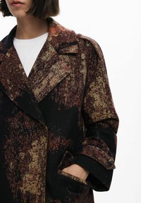 Manteau à motifs marron et noir avec une surface texturée, grand col, design croisé et poches latérales, fabriqué en tissu tissé.