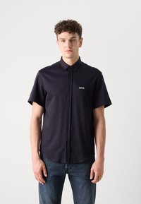 Camicia a maniche corte di colore blu navy, realizzata in tessuto morbido, con un piccolo logo bianco "BOSS" sul petto e un design del colletto classico.