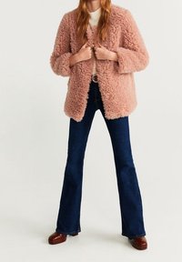 Cappotto rosa, morbido e texturizzato, con una vestibilità ampia e maniche larghe, abbinato a jeans a zampa d'elefante blu scuro e scarpe con plateau marroni.