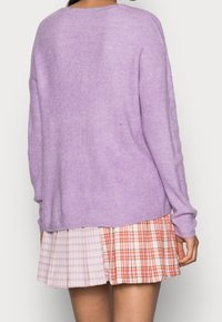 Fialový pletený svetr s žebrovanou strukturou a spadlými rameny, doplněný vícebarevnou kostkovanou sukní v odstínech růžové, oranžové a bílé.