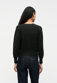 Zwarte, gebreide trui met een ronde hals, een iets cropped ontwerp en lange, losse mouwen. Gedragen met donkere denim jeans.