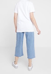 T-shirt bianco a maniche corte abbinato a jeans in denim cropped blu chiaro. I jeans hanno orli sfrangiati e sono abbinati a sneakers in tela bianca.