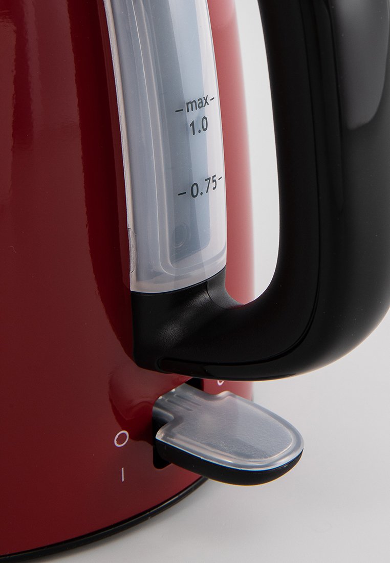 Czajnik elektryczny w kolorze czerwonym z czarną rączką, przezroczysty wskaźnik poziomu wody i przezroczysty przełącznik na podstawie. Widoczne oznaczenia maksymalnej pojemności.