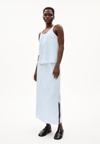 Light blue sleeveless top with a rounded neckline, paired with a matching long skirt featuring a side slit, complemented by black loafers.
