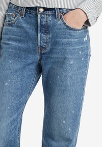 Jeans de mezclilla azul claro con un ajuste relajado, que cuentan con una cintura alta, detalles desgastados y accesorios de tono cobre.