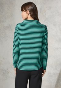Haut à rayures turquoise et noir à manches longues avec une surface texturée, dotée d'un col et d'une coupe décontractée, associé à un pantalon noir.