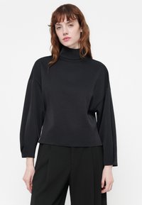 Schwarzes, langärmliges Turtleneck-Top mit lockerer Passform und weicher Textur. Der glatte Stoff fällt locker über den Körper und hat einen hohen Kragen.