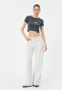 Afskåret grå t-shirt med et hvidt stjernetryk, parret med løstsiddende hvide jeans. Outfittet har diskret syninger og en afslappet pasform.