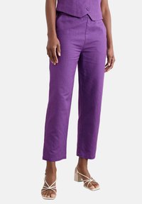 Fioletowe lniane spodnie o prostym kroju i subtelnej fakturze. W zestawieniu z beżowymi butami na obcasie z paskami dla kontrastu.