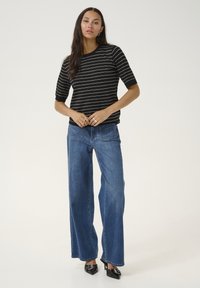 Top de manga corta a rayas blancas y negras combinado con unos vaqueros de pierna ancha azules y tacones negros de punta. La tela tiene una textura suave.