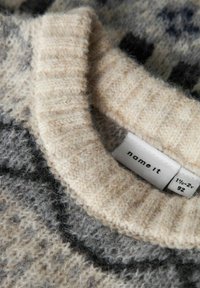 Beige kootud sviiter ribidega kaelusega, millel on hallid ja mustad mustrid. Sildil on tekst "name it," mis näitab suurust 92. Pehme, tekstuuriga kangas.
