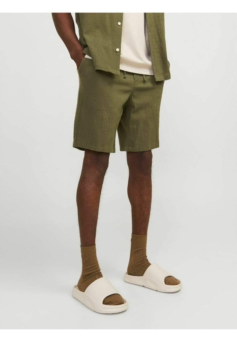 Olijfgroene gemarmerde shorts met een relaxte pasvorm, gedragen met bruine geribde sokken en lichte slidersandalen. Eenvoudig ontwerp met zakken.