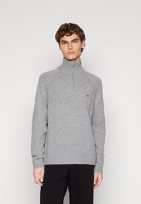 Pull-over zippé gris en matière tricotée avec un motif texturé, doté d'un col montant et de poignets et d'une taille côtelés.