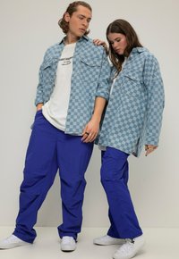 Camicie di jeans a quadri blu chiaro, t-shirt bianche e pantaloni blu vivaci. Tessuto strutturato, vestibilità ampia, con tasche visibili e dettagli con bottoni.