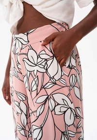Różowe kwiatowe spodnie z czarno-białym nadrukiem botanicznym, z bocznymi kieszeniami i elastycznym pasem. Gładka tekstura materiału.